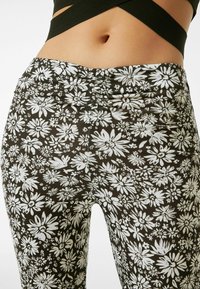 Leggings de tela negra con estampado floral blanco, con una cintura fruncida y textura suave, diseñados para comodidad y flexibilidad.