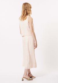 Helles rosa Zweiteiler-Outfit mit Paillettenstruktur; kurzes ärmelloses Oberteil und knielanger Rock. Goldene Absatzsandalen runden den Look ab.