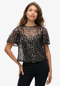 Zwarte cropped top van doorschijnende stof versierd met metalen pailletten. Heeft korte mouwen en een ronde halslijn. Textuur- en gelaagde ontwerpen.
