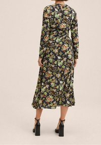 Květinové šaty s dlouhým rukávem v černé barvě se zelenými, oranžovými a bílými vzory. Mají klíčovou dírku na zadní straně a splývavou siluetu až po kotníky. Černé podpatky.