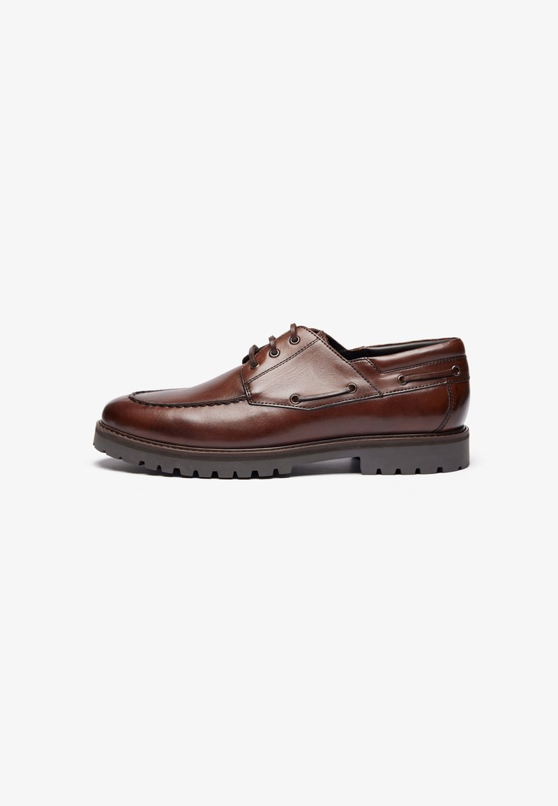 Zapato de cuero marrón con punta redondeada, diseño de cordones, cuello acolchado y suela texturizada para mayor agarre. Costuras decorativas a lo largo de los lados.