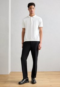 White polo shirt with short sleeves and a collar, paired with black tailored pants and black shoes featuring a textured sole.