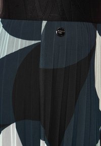 Gonna plissettata con motivo geometrico in blu navy, nero e bianco, con una fascia testurizzata e un bottone in metallo nero in vita.