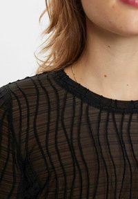 Top nero trasparente con texture a coste verticali, scollatura rotonda e bordo arricciato lungo i lati. Tessuto sottile e delicato.