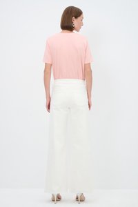 Light pink short-sleeve t-shirt paired with white wide-leg pants. Smooth fabric with a relaxed fit. Silver heels complete the outfit.