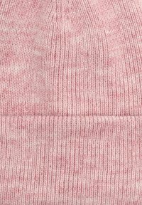 Nahaufnahme von weichem, rosa gestricktem Stoff mit einem gefalteten Rippenrand, der ein feines, gleichmäßiges Stichmuster zeigt.