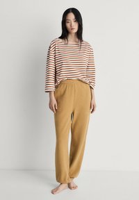 Gestreepte longsleeve shirt in wit en roest, gecombineerd met beige sweatrpanten. De broek heeft een elastische tailleband en taps toelopende boorden.