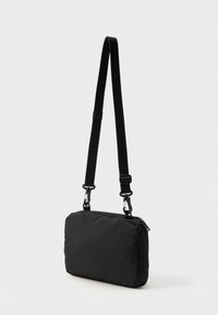 Čierna obdĺžniková taška na rameno s textúrovaným povrchom, nastaviteľným popruhom a dvojitými kovovými klipsami. Zips na vrchu.