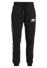 Schwarze Baumwoll-Sweatpants mit einem Kordelzugbund, gerippten Bündchen und einem weißen Branding-Detail entlang des linken Beins. Weiche Textur.