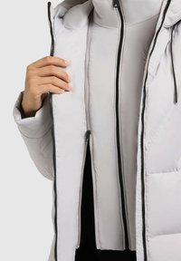 Šviesiai pilkas pūkinis švarkas su dvikryptiniu užtrauktuku, turintis lygų paviršių ir gobtuvą, demonstruojantis vidinį pamušalą ir juodas užtrauktuko akcentus.