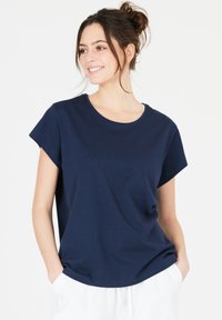 Mörkblå, kortärmad t-shirt i mjuk bomull, med rund halsringning och avslappnad passform, bärs med vita byxor.