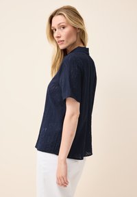 Navyblauwe korte mouwen shirt van een gestructureerde, gemusterde stof met een subtiele kraag, gecombineerd met witte broek.