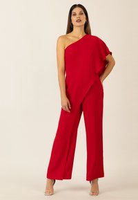 Jumpsuit rosso a spalla singola con manica a volant fluente, design a gamba larga e texture liscia, completato da tacchi a strappo argentati.