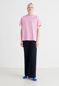 Camiseta de algodón rosa de manga corta y corte relax, combinada con pantalones de mezclilla oscuros de pierna ancha y zapatillas azules de slip-on con rayas.