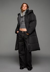 Giacca a vento nera con cappuccio, maglione grigio a maglia e jeans neri a gamba larga. Tessuto liscio, design fino al ginocchio e dettagli in hardware argentato.