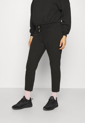 Schwarzes gesteppte Sweatshirt mit passenden tapered Hosen; beide haben eine geometrische Textur und elastische Bündchen. Kombiniert mit schwarzen Sportschuhen.