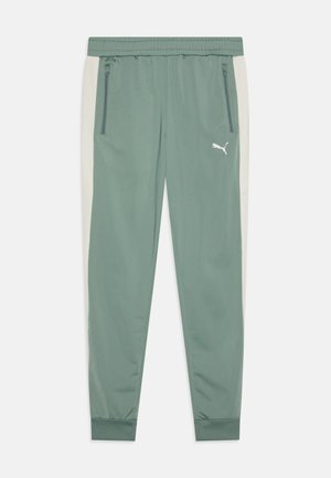 Pantalons de survêtement verts avec des panneaux latéraux beiges clairs contrastants, ceinture élastique, poches zippées et un logo Puma blanc sur la cuisse gauche.