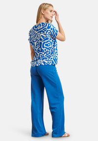 Blue patterned short-sleeve top with abstract shapes paired with solid blue wide-leg pants. Smooth fabric, relaxed fit.