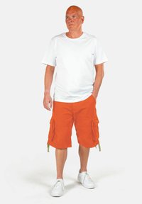 Maglietta bianca in cotone, pantaloni cargo arancioni con tasche e sneaker bianche. I pantaloni corti hanno legature laterali. Design semplice e casual.