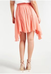 Jasnoróżowa spódnica w stylu high-low, wykonana z lekkiego materiału, z fakturowanym, marszczonym paskiem w talii oraz koronkowymi detalami wzdłuż szwów.