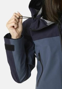 Marineblå og grå softshell jakke med en lynlåslomme, justerbar hætte med snoretræk og Velcro-manchetlukning. Glat tekstur.