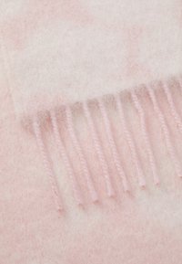 Lyserød uldkast med blød tekstur. Har frynser i kanten lavet af matchende garn, der viser en subtil gradient-effekt.