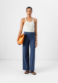 Débardeur blanc à rayures, pantalons larges navy, sac à main géométrique orange, tongs noires. Design simple avec des couleurs et textures contrastées.