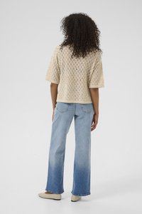 Beige strikbluse med diamantmønster, korte ærmer, parret med lyseblå vidde jeans med en lys-til-mørk gradient.