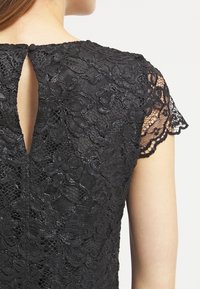 Svart spetsklänning med blommönster, korta skålarm och en nyckelhålsrygg som knäpps med en knapp.