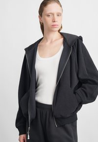 Svart zip-up hettegenser i myk stoff, med en avslappet passform, store frontlommer og en dekorativ glidelås med perler.