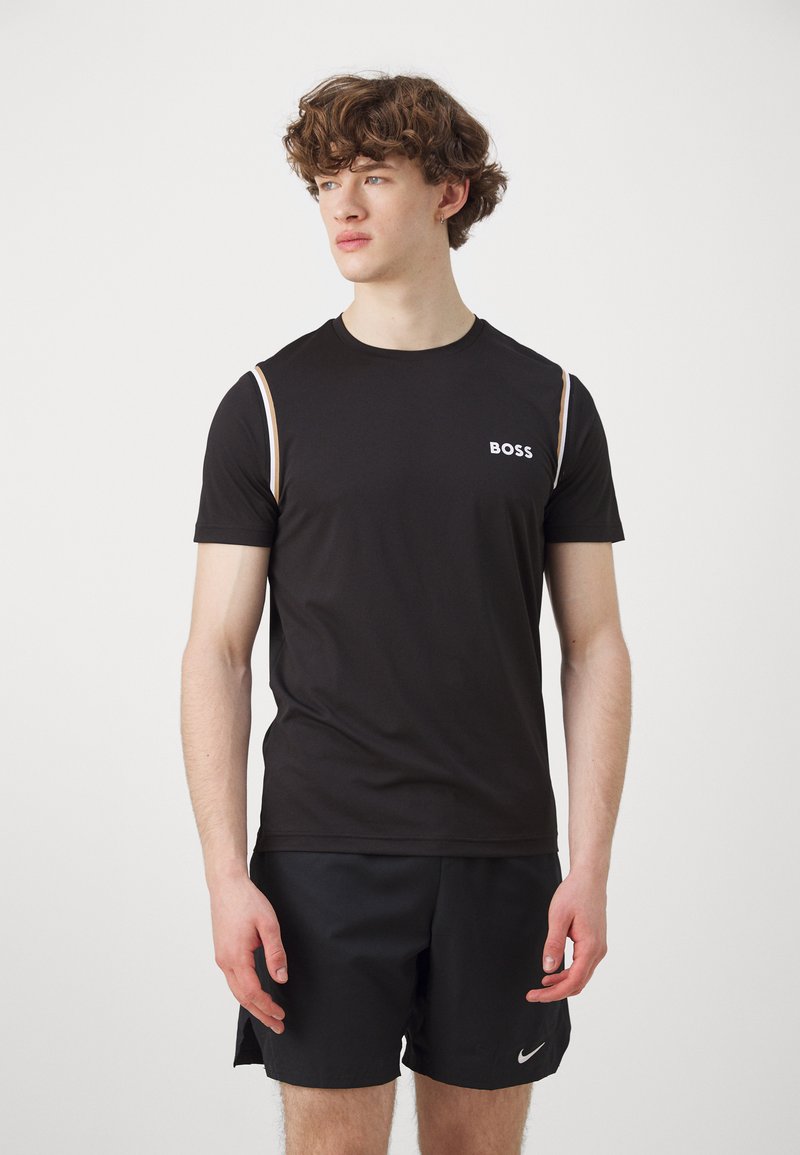Camiseta atlética negra de manga corta, con un logo blanco de "BOSS" y rayas de hombro en un tono beige que contrastan. Tela suave y transpirable.