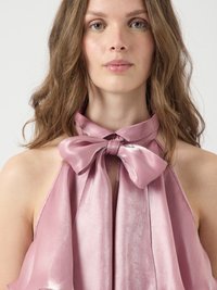 Rosa satinblus med en rosettdetalj vid halsen, med en flödande, texturerad design som mjukt faller över axlarna.