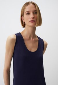 Granatowa, bezrękawnikowa bluzka z okrągłym dekoltem, wykonana z gładkiego, lekkiego materiału, o luźnym kroju i bez widocznych wzorów czy akcentów.