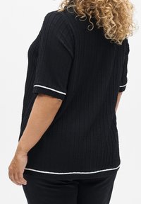 Czarny top z fakturą, z prążkowanym wzorem, krótkimi rękawami z białą lamówką i zaokrąglonym dołem. Widok od tyłu ukazuje kształt ubrania.