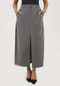 Szara, wysoka spódnica maxi z rozcięciem z przodu, bocznymi kieszeniami i subtelnym wzorem w paski; połączona z czarnymi butami na szpilkach.