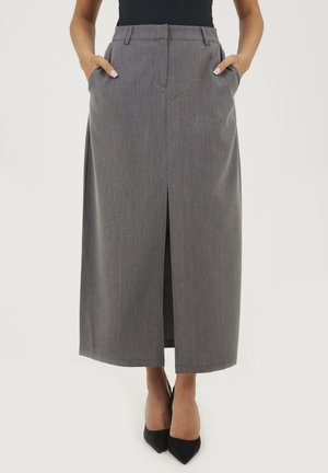 Jupe maxi grise taille haute avec une fente sur le devant, des poches latérales et un motif rayé subtil ; associée à des chaussures noires à bout pointu.