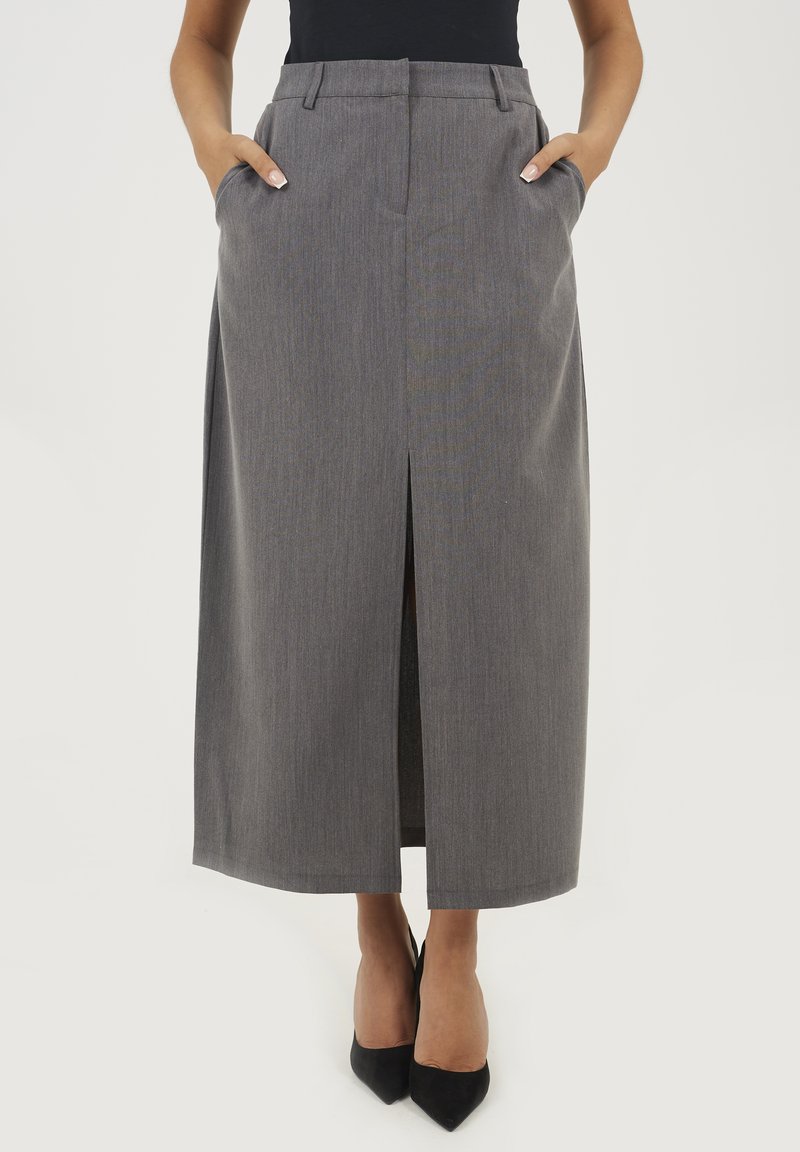 Szara, wysoka spódnica maxi z rozcięciem z przodu, bocznymi kieszeniami i subtelnym wzorem w paski; połączona z czarnymi butami na szpilkach.