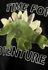 Maglietta nera in tessuto con grafica di un dinosauro verde con spine testurizzate, accompagnata dal testo "È TEMPO DI AVVENTURA" in bianco.
