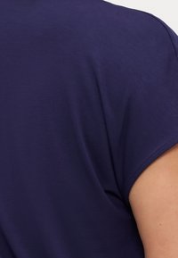 Närbild av en persons överarm som bär en kortärmad, mörkblå skjorta som visar tygtextur och sömdetaljer.