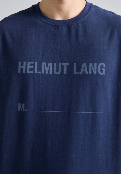 Marineblå bomulls t-skjorte med teksten "HELMUT LANG" i fet hvit skrift og "M. _____" trykt under i lysere skrift.