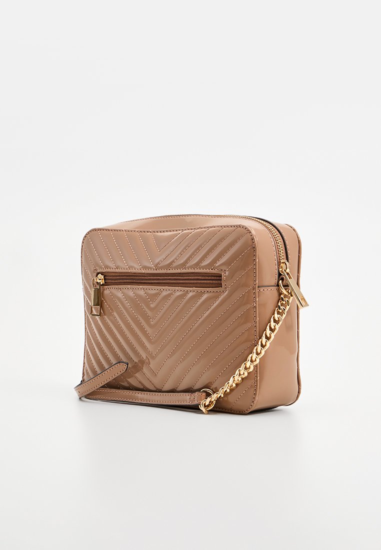 Sac à main capitonné beige avec un motif en chevron, une bandoulière en chaîne dorée, une poche arrière zippée et une finition lisse et brillante.