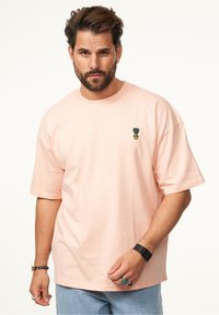 Rosa Baumwoll-T-Shirt mit kurzen Ärmeln, das ein kleines gesticktes Ananasdesign auf der linken Brust aufweist. Lockere Passform und weicher Stoff.