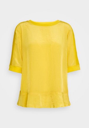 Blouse jaune à manches courtes avec encolure ronde, coupe légèrement ample et détail subtil de volants à l'ourlet.