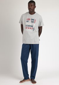 Camiseta gris con texto multicolor que dice "Lois: Una de las principales marcas de jeans del mundo." Combinada con pantalones azul marino.