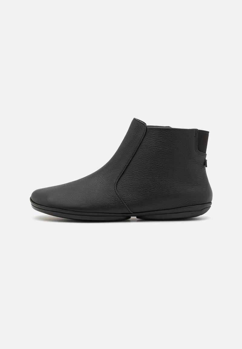 Bottine en cuir noir avec bout arrondi, semelle plate et panneau élastique latéral pour un chaussant facile, sur fond neutre.