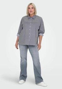 Camisa de botones a rayas con cuello, mangas enrolladas y un ajuste holgado, combinada con vaqueros de campana azules claros y zapatillas blancas.