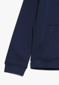 Sudadera de color azul marino con un acabado texturizado, que cuenta con un bolsillo tipo canguro y puños de canalé. Los detalles de costura añaden estructura.