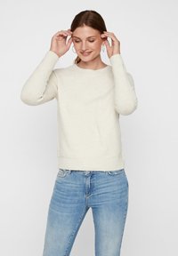 Vaalea beige neulepusero, jossa on pyöreä pääntie ja ribbireunukset. Yhdistettynä vaaleansinisiin farkkuihin, tekstuuri näyttää pehmeältä ja mukavalta.