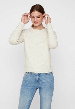 Light beige knitted sweater with a crew neckline and ribbed cuffs. Paired with light blue denim jeans, the texture appears soft and cozy.