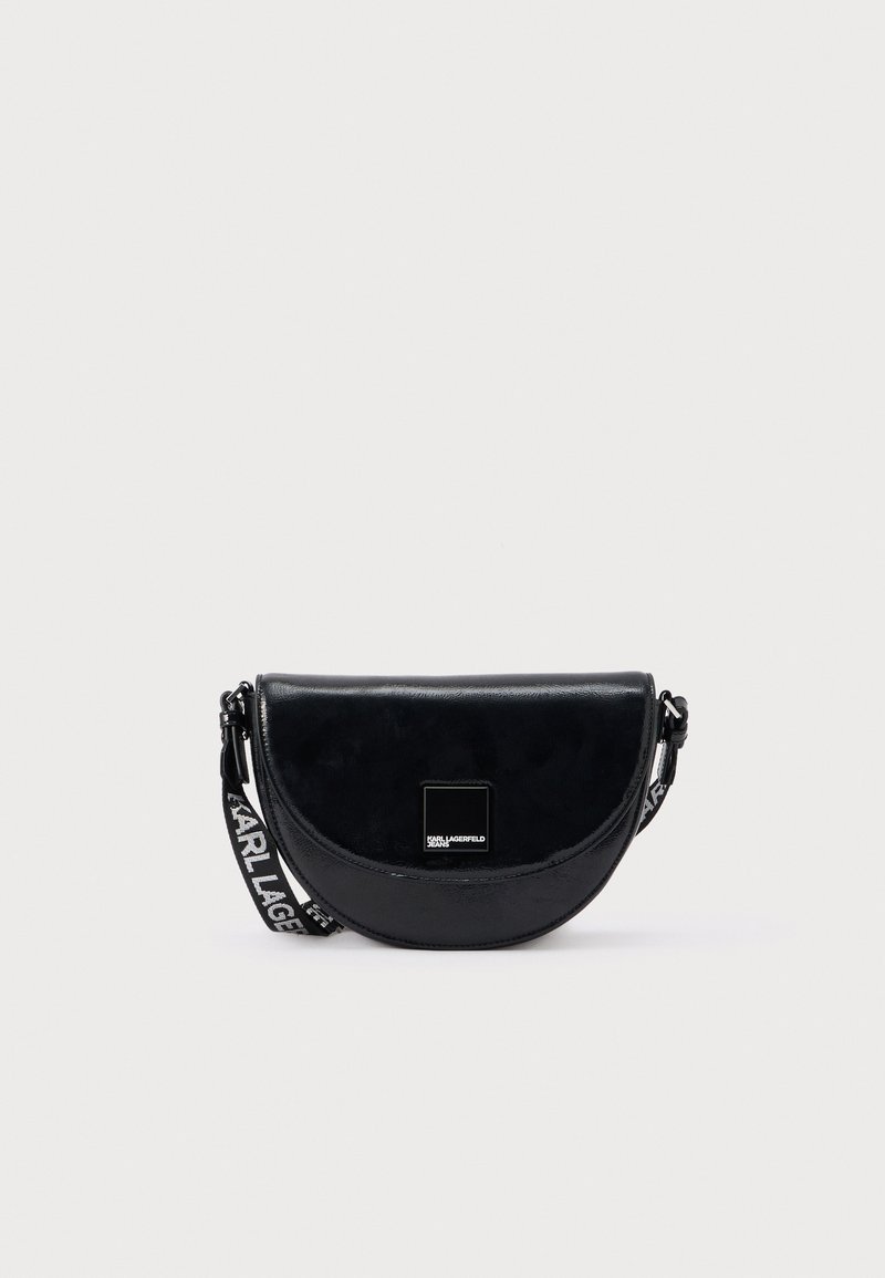 Černá kožená kabelka přes tělo ve tvaru půlměsíce, s lesklým povrchem a popruhem s logem pro nastavitelnou délku nošení.